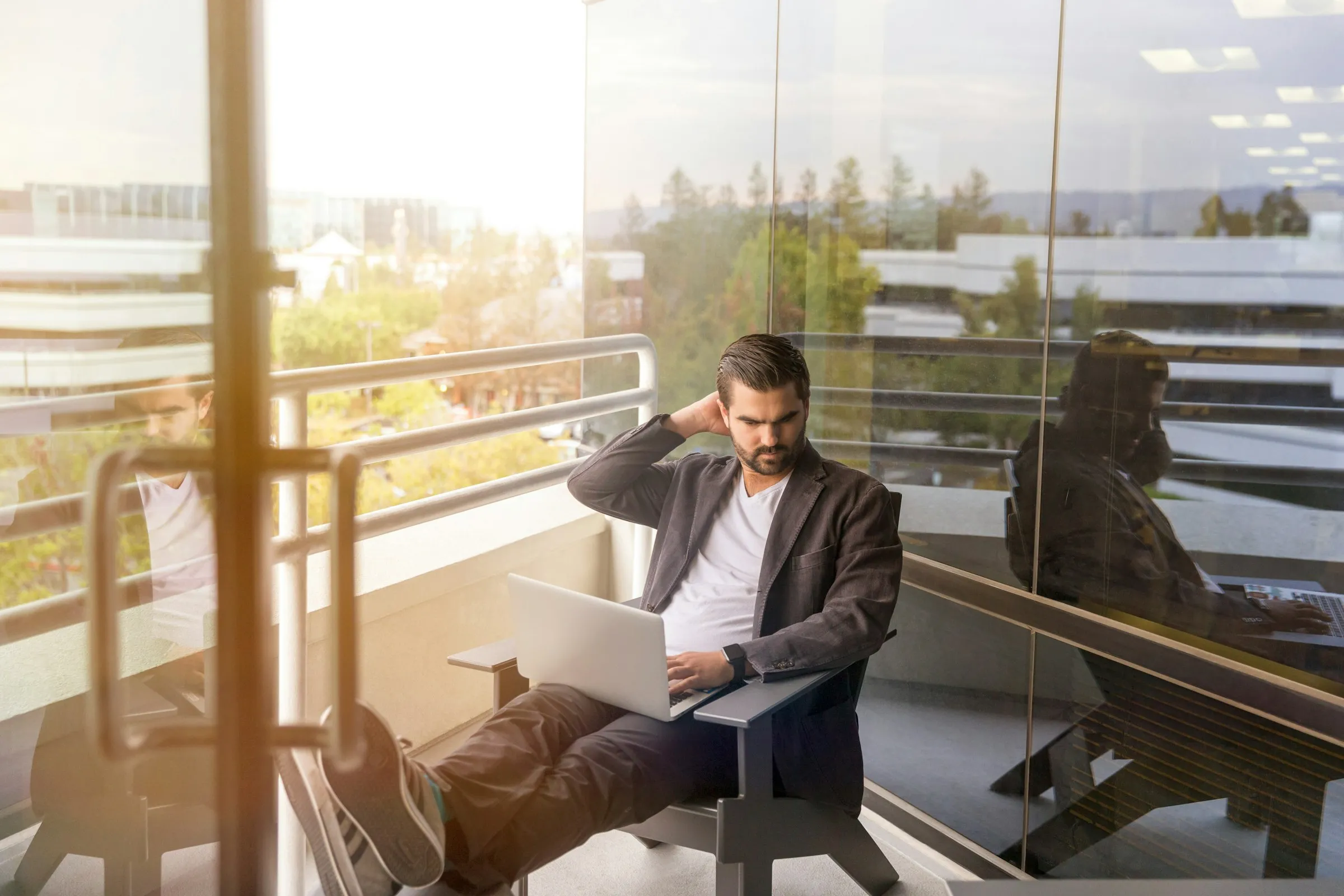 An investor working on a laptop on a sunny office balcony